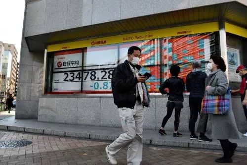 ▲2月21日，在日本东京，路人走过街边的电子股指信息显示屏。（新华社/法新）