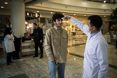 3月5日，在伊朗德黑兰，一名安保人员为进入商场的顾客测量体温。新华社发（艾哈迈德·哈拉比萨斯摄）