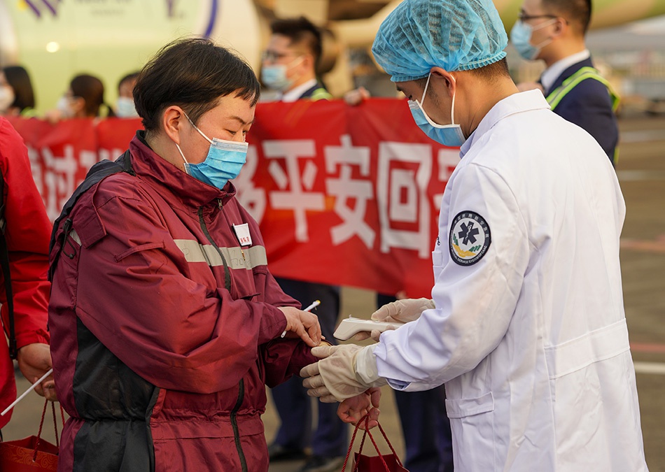 3月18日,在重庆江北国际机场,工作人员为重庆援鄂医疗队首批返回的医护人员检测体温。新华社记者 刘潺 图