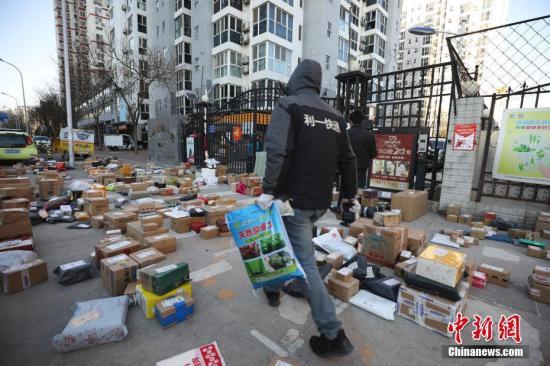 资料图:快递员为居民查找搬运快递物品。中新社记者 赵隽 摄