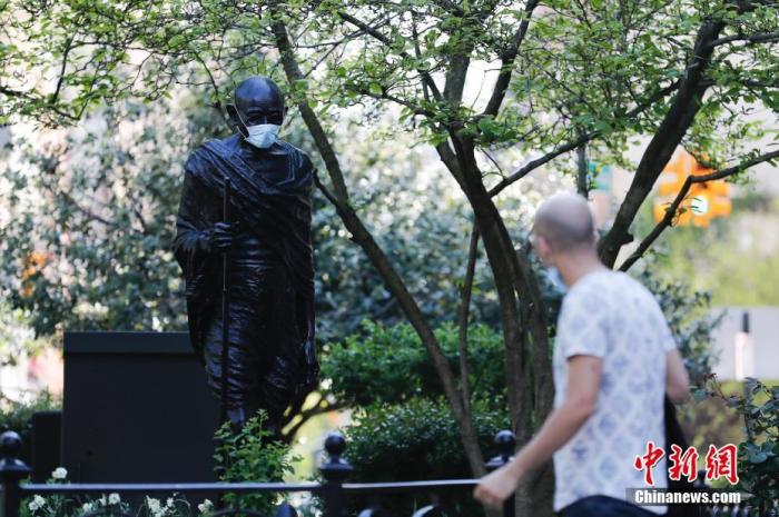  资料图：当地时间5月3日，有人为纽约联合广场的甘地雕塑戴上口罩，引起许多路人注目。 中新社记者 廖攀 摄