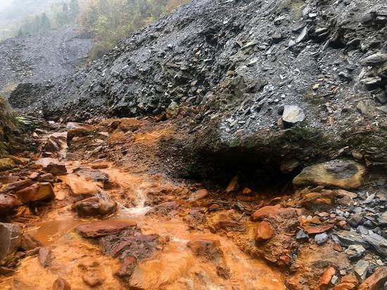 安康市白河县凤凰村露天堆放的矿渣随处可见，有矿渣的地方流水就呈土黄色，PH值显示为强酸性。