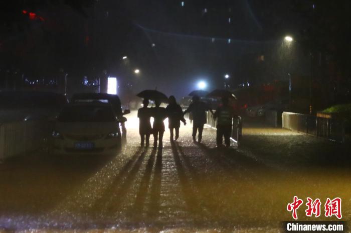 7月7日晚，江西南昌，民众在汽车灯光的照射下冒雨前行。　刘占昆 摄