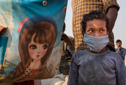 5月18日，在印度新德里郊区的加济阿巴德，一名儿童和家人一起排队等待登上返乡大巴。新华社发