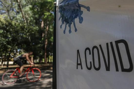 8月26日，在巴西圣保罗市一家公园，一名男子骑车经过写有“冠状病毒”字样的横幅。新华社发（拉赫尔·帕特拉索摄）