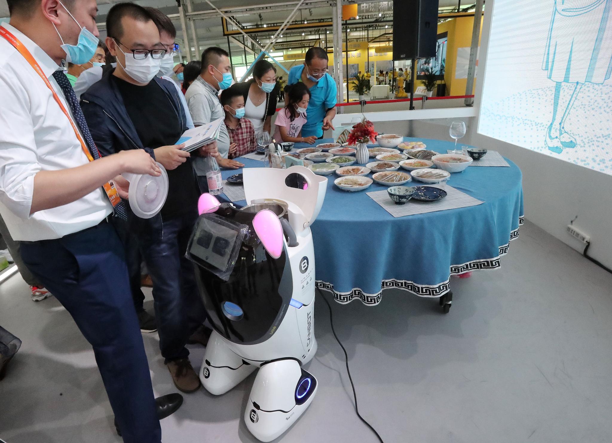  现场工作人员向观众介绍机器人及其制作的菜品。新京报记者 王贵彬 摄