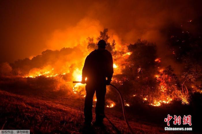 资料图:当地时间9月15日,美国加州,消防员站在消防车上观看山猫大火在蒙罗维亚房屋后的山坡上燃烧。