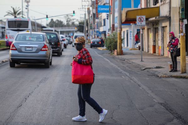  1月8日，在墨西哥墨西哥州内萨瓦尔科约特尔城，一名女子戴口罩穿过马路。（新华社）